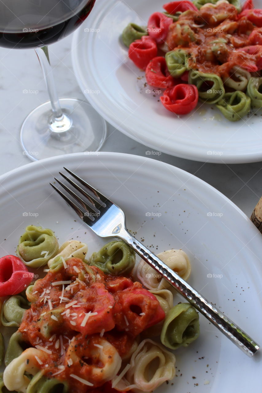 Italian inspired meal of tri-colored tortellini with red sauce and red wine.