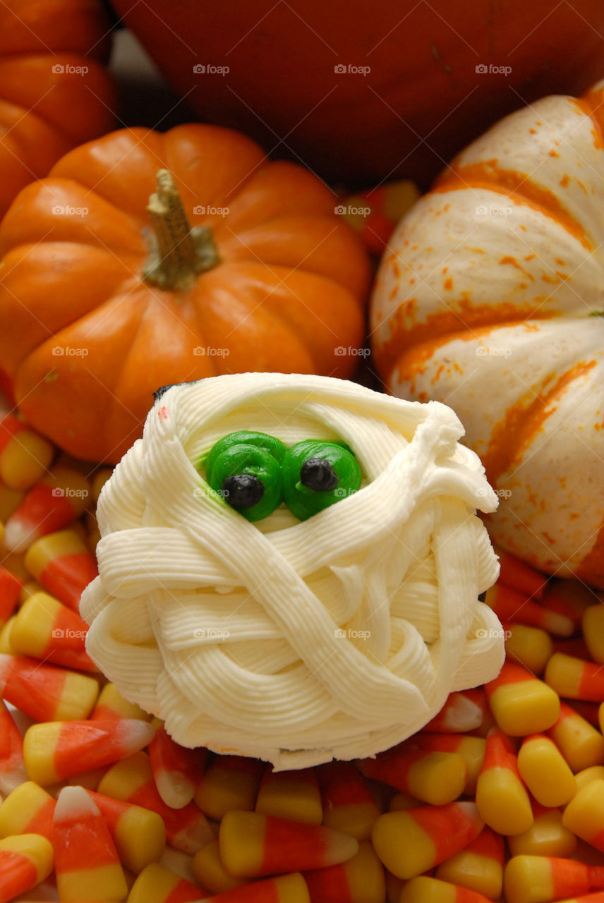 A sweet and scary “mummy” cupcake sitting on some candy corn perfect for Halloween!