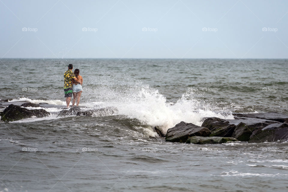 A romantic couple of young people on a stone mole on the ocean coast.