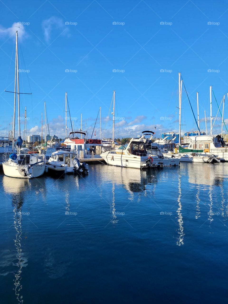 Mirror reflection of boats in ocean on a bright clear blue sky day, docks in fishermans wharf, Victoria, British Columbia, Canada.