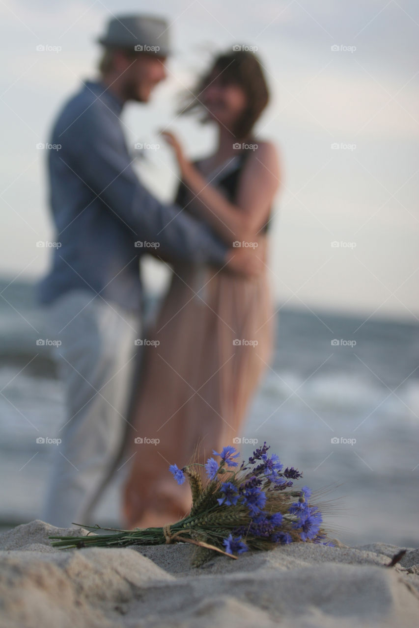 Blue bridal bouquet with unsharp wedding couple in background, at the beach