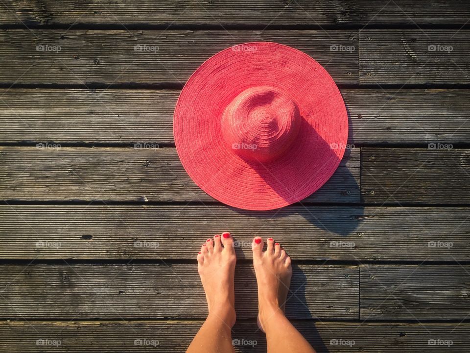 Looking down at woman's feet and pink summer hat on wooden pontoon