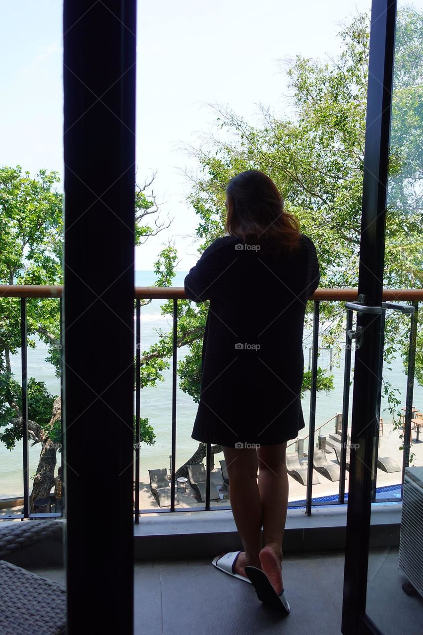 asian woman standing looking at the vast sea from the hotel balcony