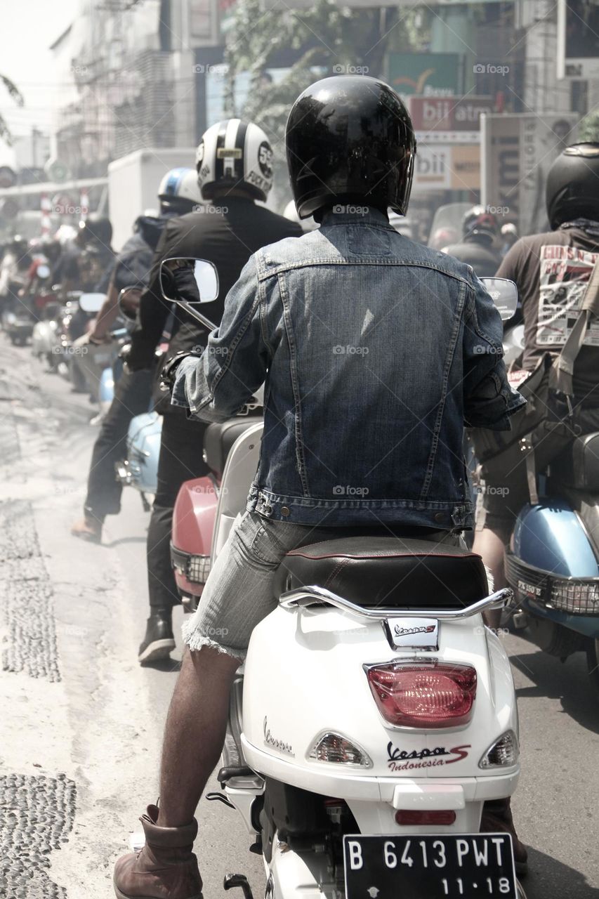 Portrait of a white scooter rider in a jeans jacket riding an automatic Vespa stuck in a traffic jam on a street in Jakarta, Jakarta, Indonesia.