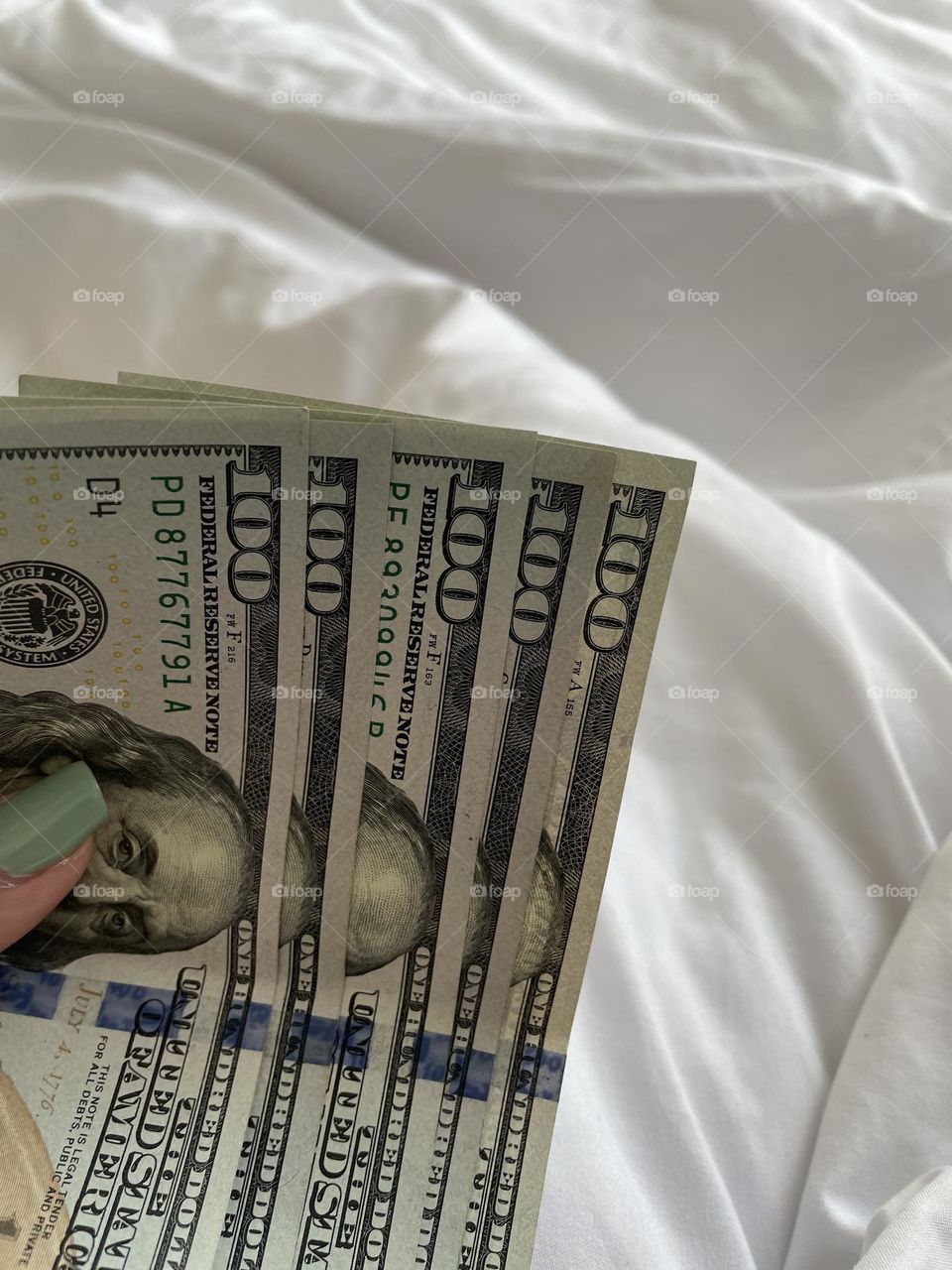 Holding dollar cash over white bed sheet