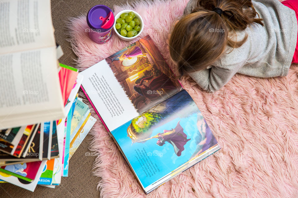 Girl reading her book in bedroom with stack of books showing love for reading and knowledge. Staying in good shape starts from a young age. Stimulate the mind. Healthy snacks for a healthy lifestyle.