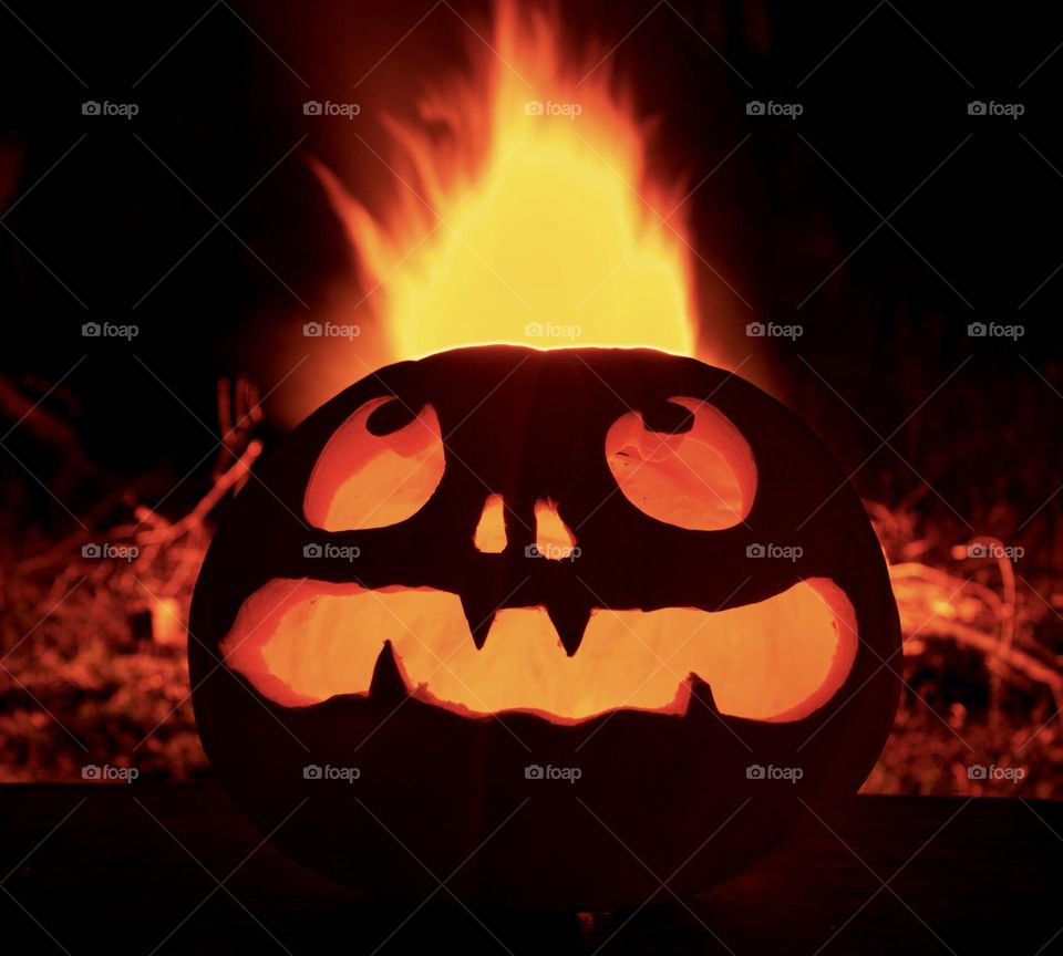 A carved pumpkins in front of a bonfire, giving it the appearance of flaming hair