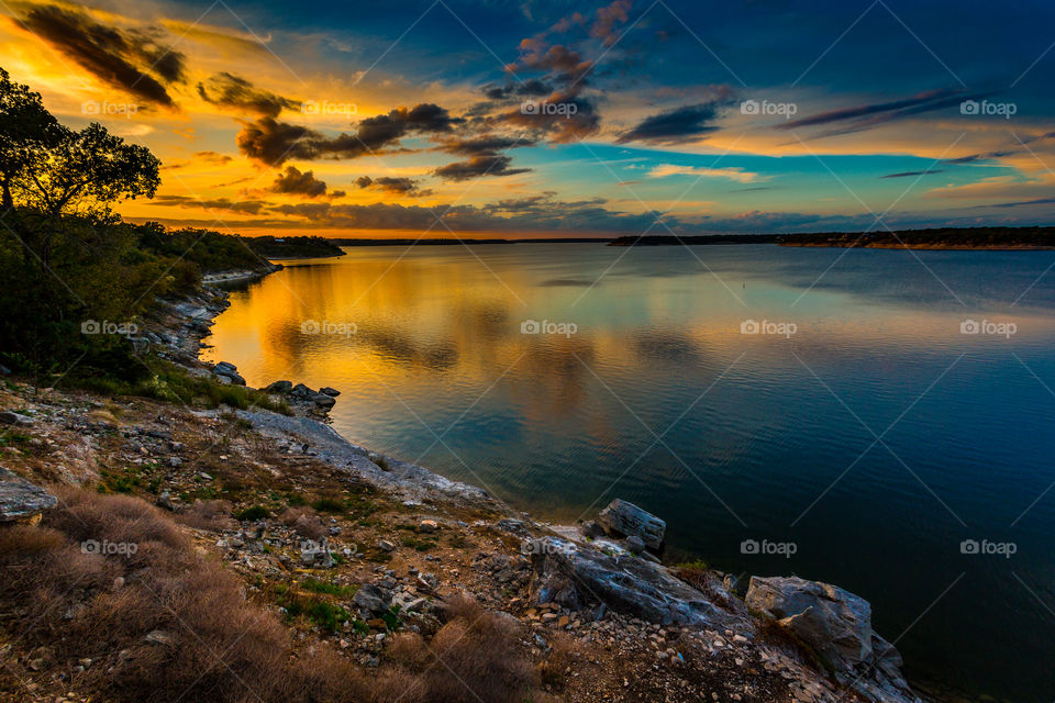 The evening sun sets over a rock covered lake shore creating a beautiful orange glow in the clouds