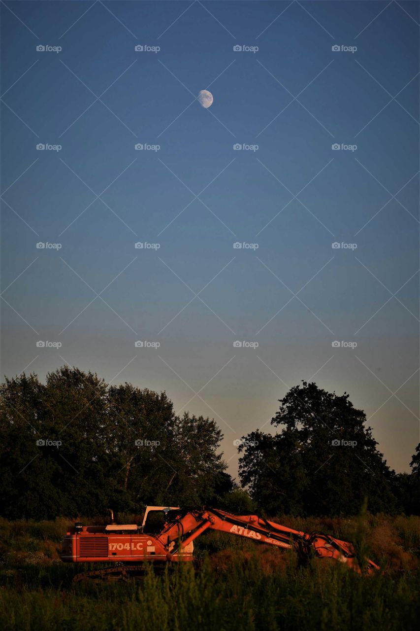 Excavator at an abonded construction site under a clear sky with moon