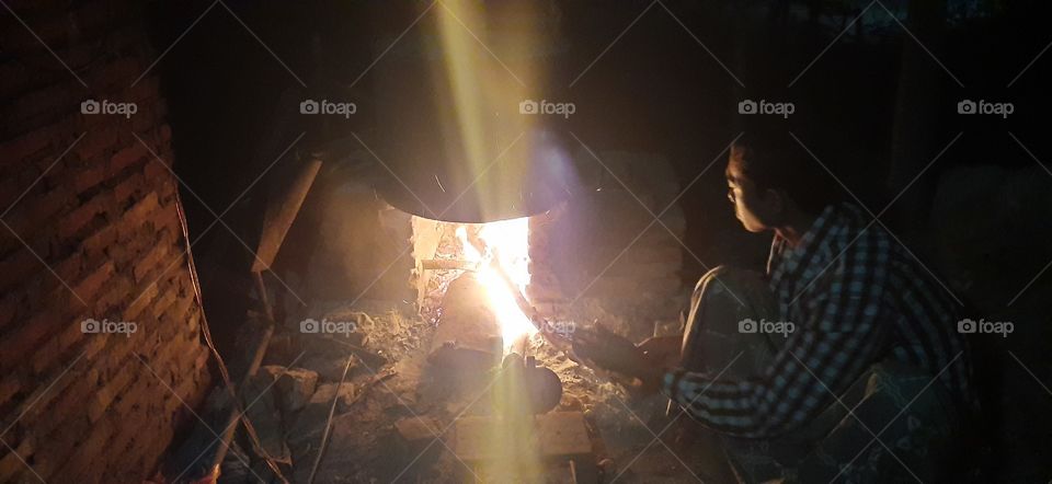 A boy is lighting a fire to heat water in an iron stove