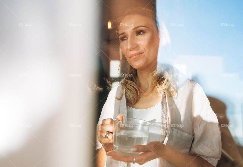 Young adult woman blonde long hair with glass of water on morning kitchen at the home, healthy lifestyle