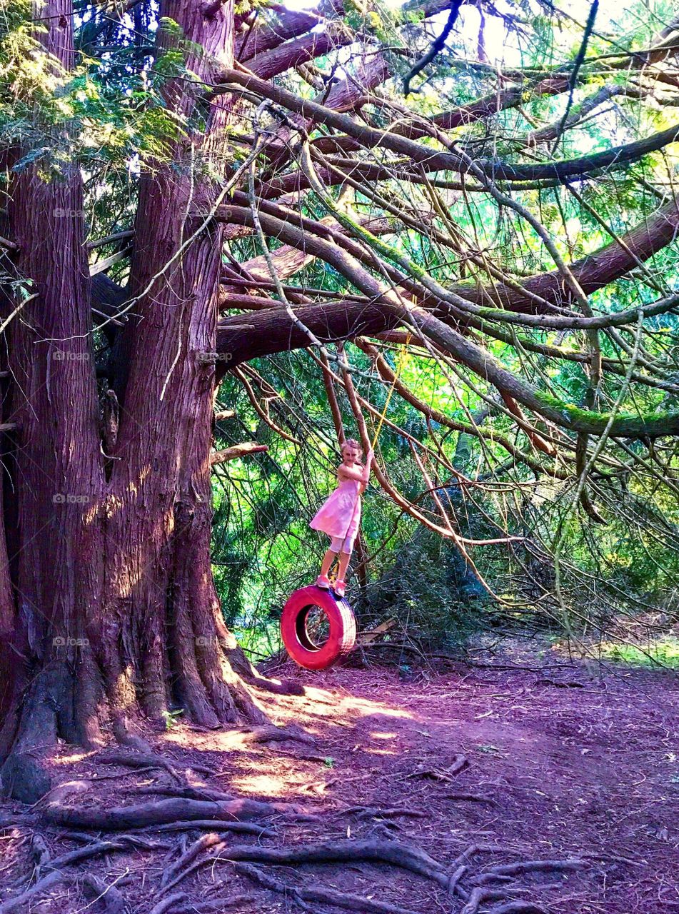 Girl swinging on pink-painted tire swing in dense forest 