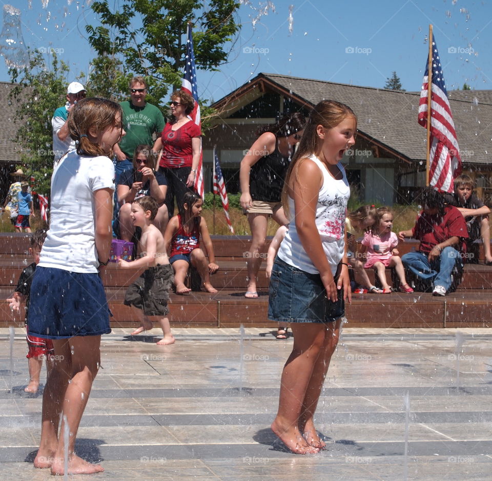 Two girls express total joy and surprise as they are hit with water jets while playing in a fountain ar Centennial Park in Redmond in Central Oregon on a sunny summer day.