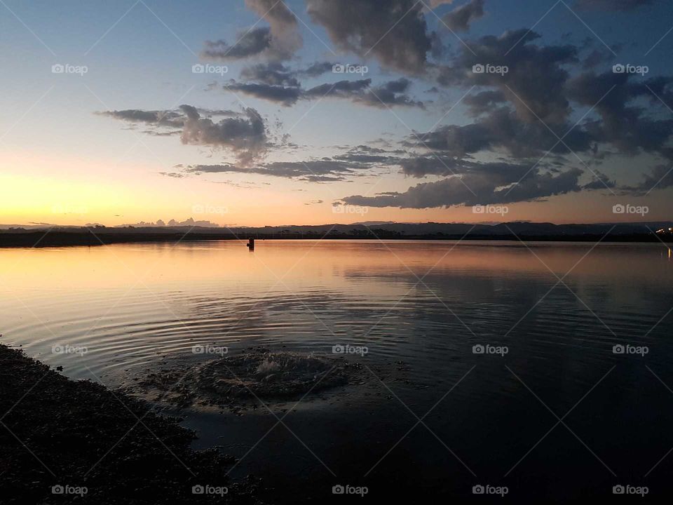 A beautiful scene of the sunset over pandora pond in Napier. A splash as a rock hits the water is visible in the water causing circular ripples in the water.