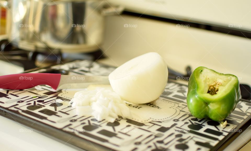 Fresh onions and bell peppers on a cutting board pot cooking in background 