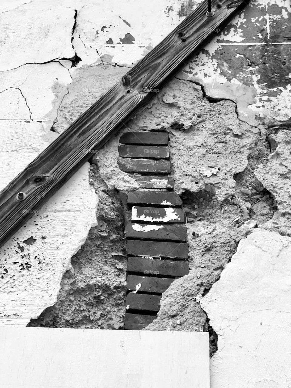 Monochromatic close up of crumbling walk with exposed brick column and board