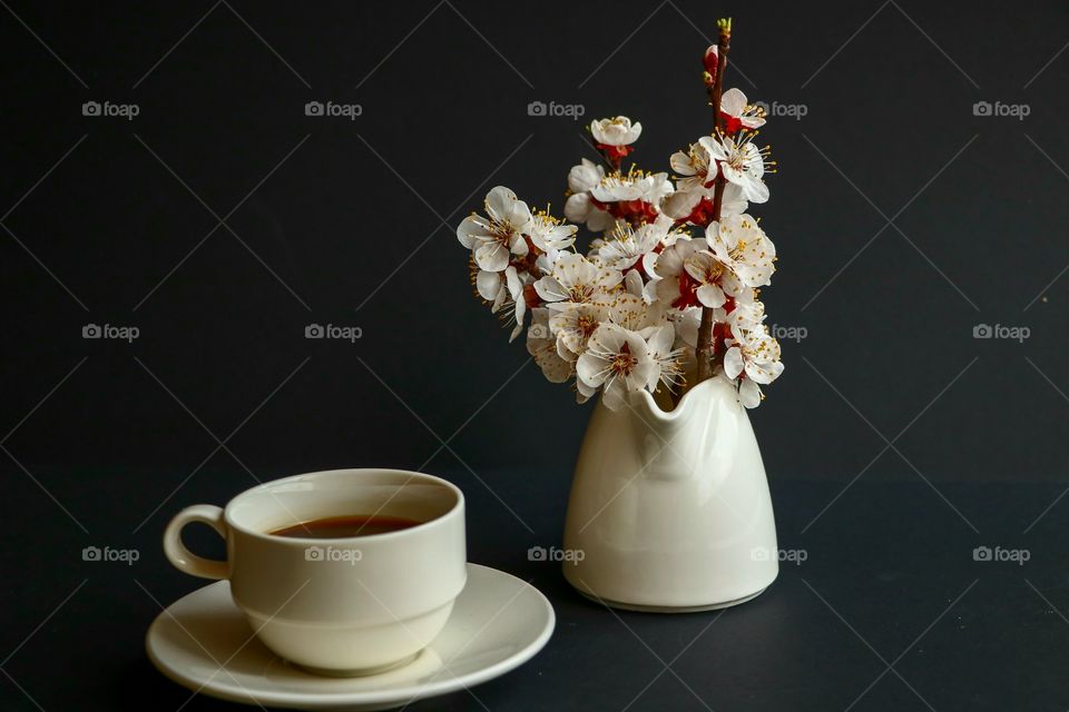 Still life made by cup with black coffee and some spring flowered branches in the white jug.