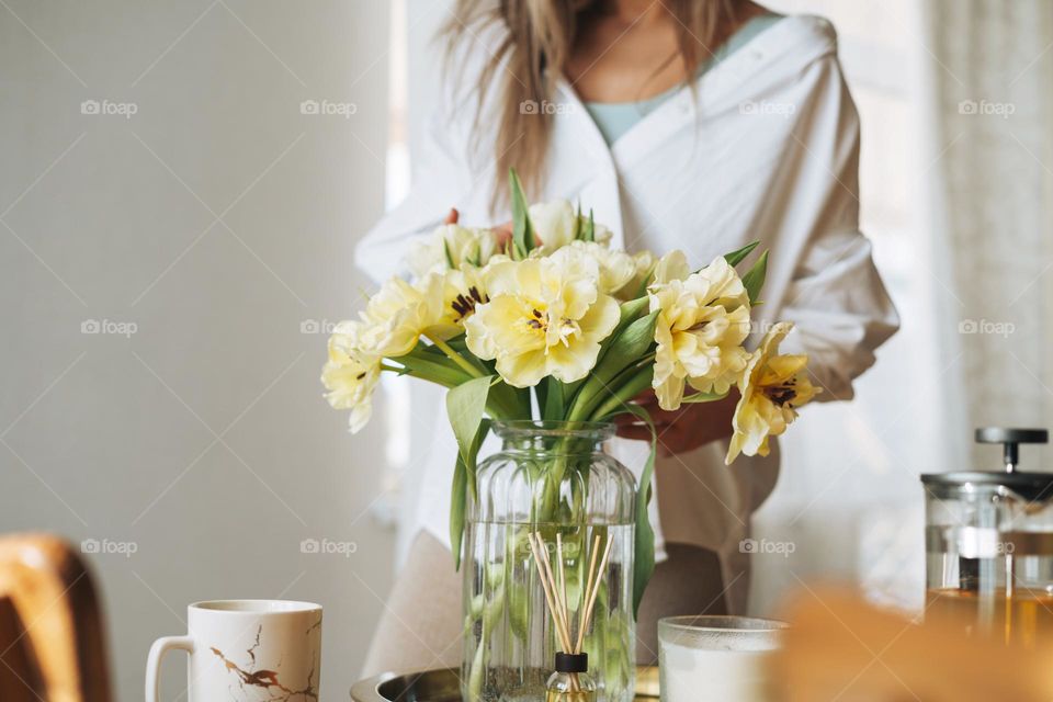 Bouquet of flowers yellow tulips in vase in woman hands on table at home 