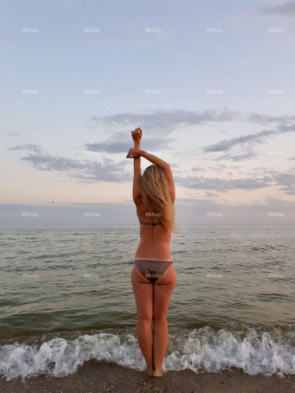 Faceless woman in swimming suit stands alone at the evening beach 