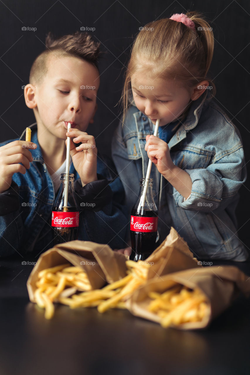 beautiful brother and sister of Caucasian nationality, at home, drinking Coca-Cola, laughing, rejoicing, hugging and having fun.  Happy kids dressed in denim clothes.  beautiful advertisement.  Lifestyle photo