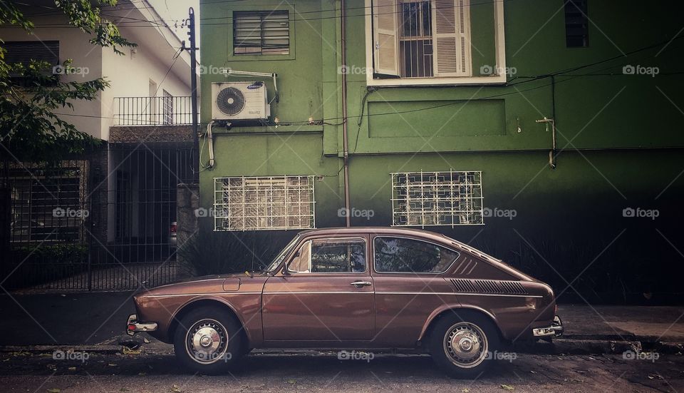 Old brown car parked in a simple neighborhood 