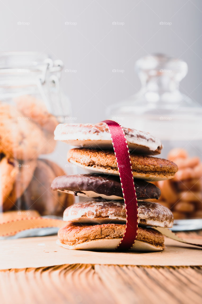 A few gingerbread cookies wrapped in red ribbon Happy Christmas on wooden table. Jars with sweets in the background