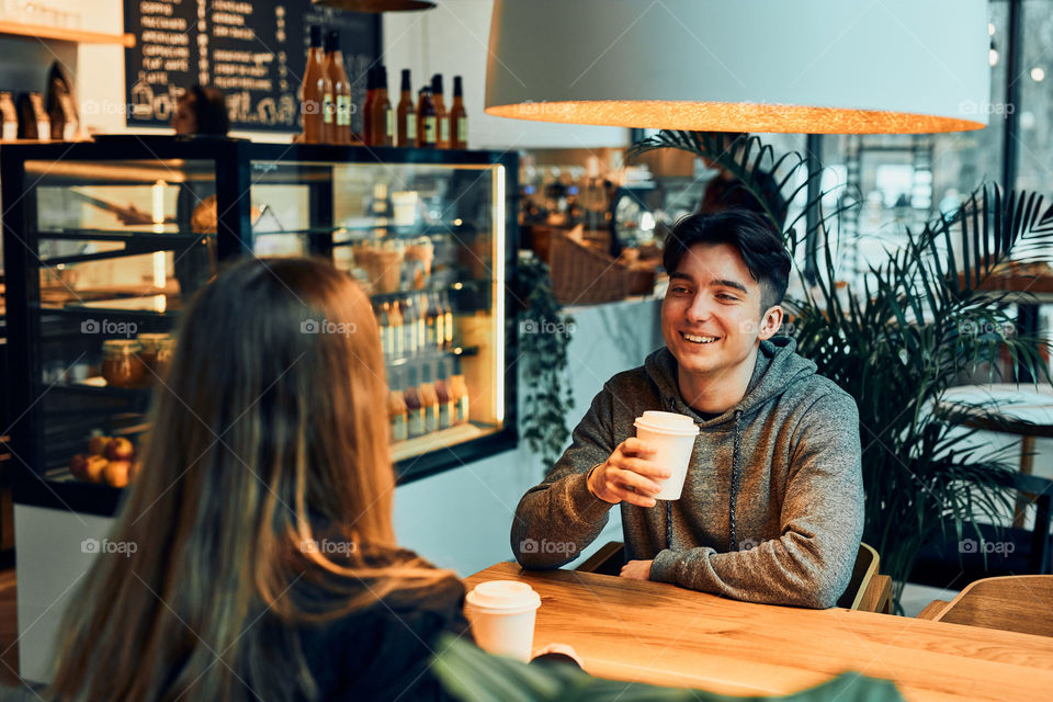 Friends having a chat, talking together, drinking coffee, sitting in a cafe. Young man and woman having a break, relaxing in cafe