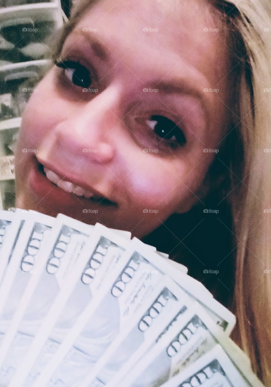 young woman holding a stack oh one hundred dollar bills taking a selfie